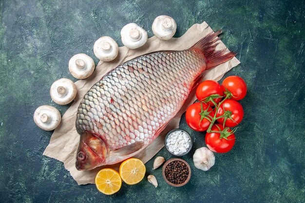 bovenaanzicht verse rauwe vis met rode tomaten en schijfjes citroen op donkerblauwe achtergrond