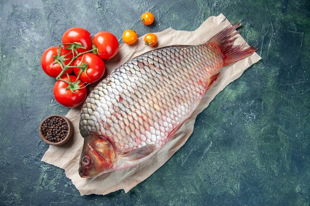 Bovenaanzicht verse rauwe vis met rode tomaten op donkerblauwe achtergrond