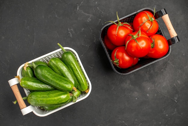 Bovenaanzicht verse rode tomaten met komkommers in manden op de donkere achtergrond