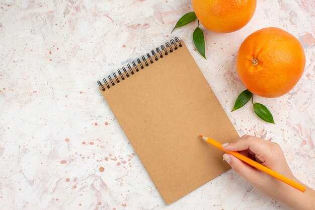 Bovenaanzicht verse sinaasappels een blocnote potlood in vrouwelijke hand op lichte oppervlak vrije plaats