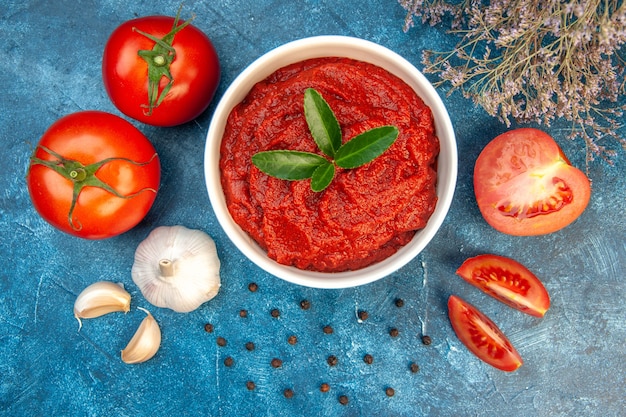 Bovenaanzicht verse tomaten met tomatenpuree en knoflook op blauwe tafel