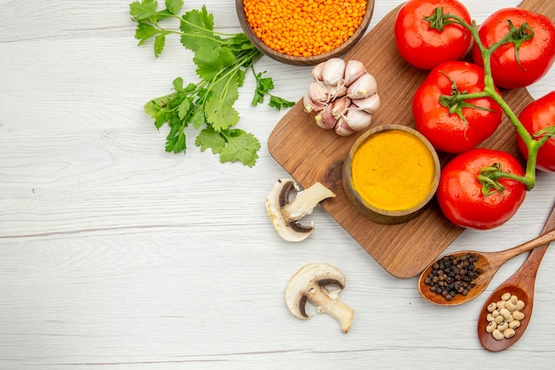 Bovenaanzicht verse tomatentak knoflook kurkuma kom op snijplank champignons linzen kom peterselie op grijze tafel