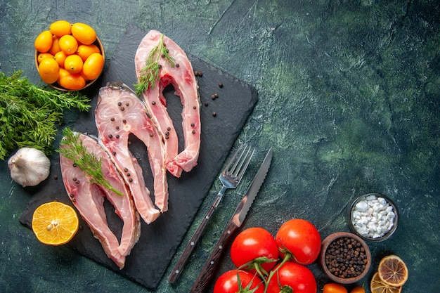 bovenaanzicht verse vis plakjes met groene rode tomaten en kumquats op donkere achtergrond