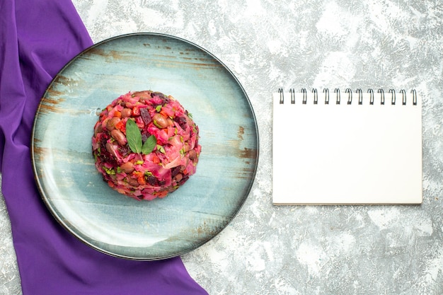 Bovenaanzicht vinaigrette bietenaardappelsalade op ronde plaat paarse sjaal notebook op lichttafel