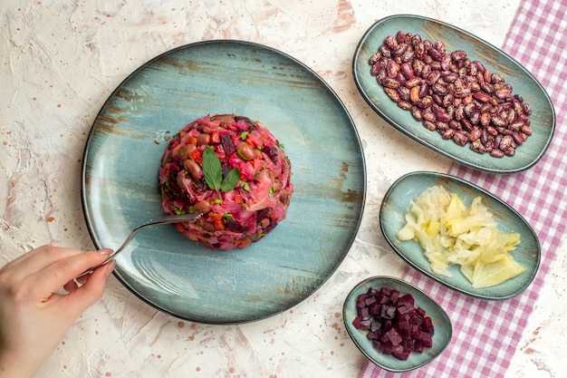 Bovenaanzicht vinaigrette salade op ronde plaat gepekelde kool bonen gesneden bieten op platen vork in vrouwelijke hand op lichtgrijze tafel