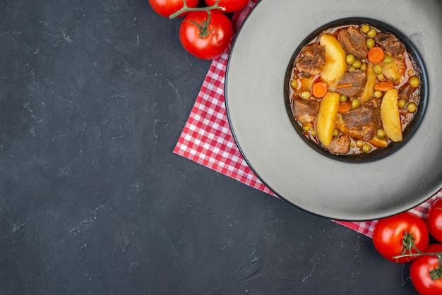 Bovenaanzicht vleessoep met garnituur op ronde plaat verse tomaten op zwarte tafel met vrije ruimte