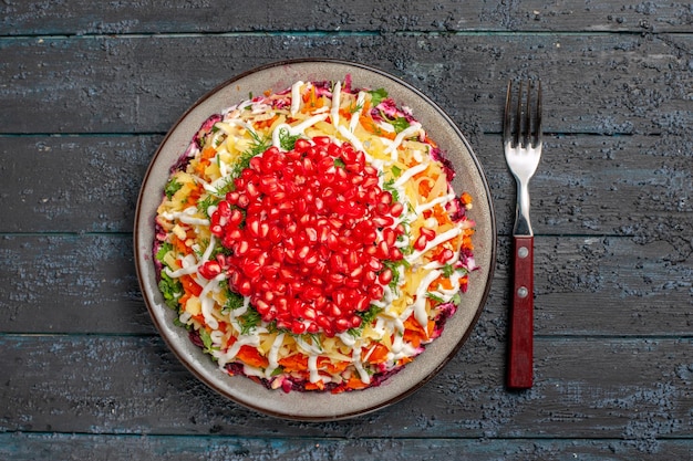 Bovenaanzicht voedselschaal met zaden van granaatappel en mayonaise naast de vork op de grijze tafel