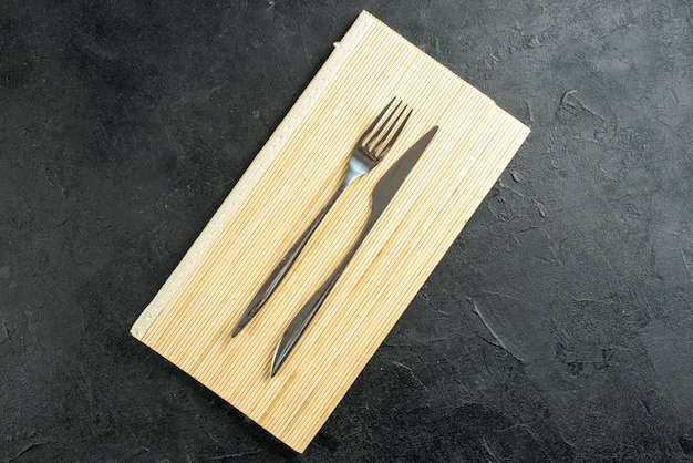 Bovenaanzicht vork en mes op beige houten bord op zwarte tafel met vrije ruimte