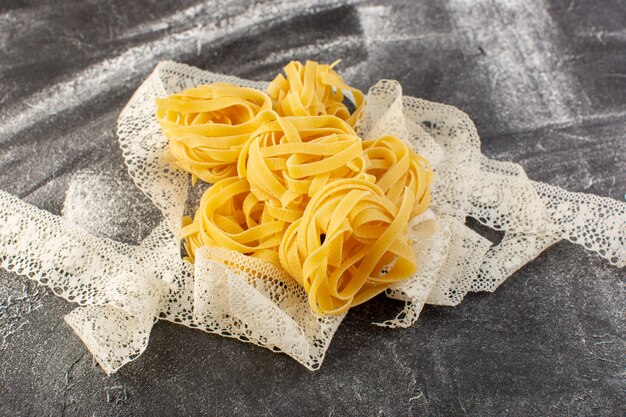 Bovenaanzicht vormde Italiaanse pasta in bloemvorm rauw en geel met weefsel op de grijze achtergrond Italiaanse rauwkost maaltijd spaghetti