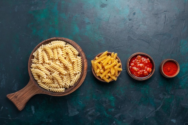 Bovenaanzicht vormde italiaanse pasta met saus en kruiden op het donkerblauwe bureau