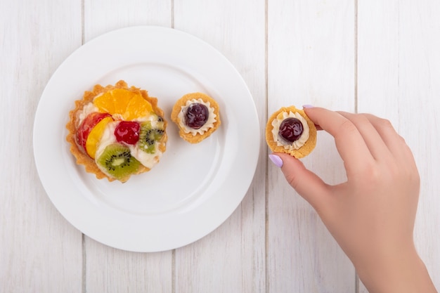 Bovenaanzicht vrouw eten met taartjes op een plaat op witte achtergrond