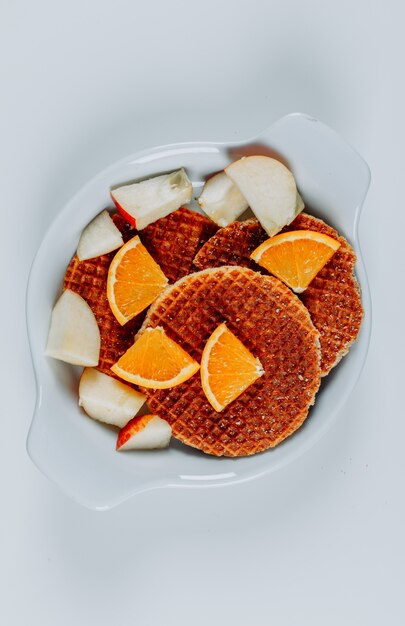 Bovenaanzicht wafels in kom met sinaasappelen en appels op witte achtergrond. verticaal