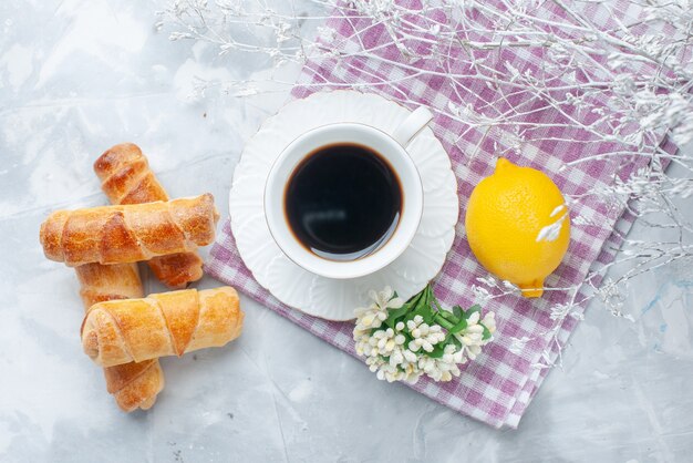 Bovenaanzicht zoete armbanden met vulling samen met koffie en citroen op de lichte vloer gebak bakken zoete koffie