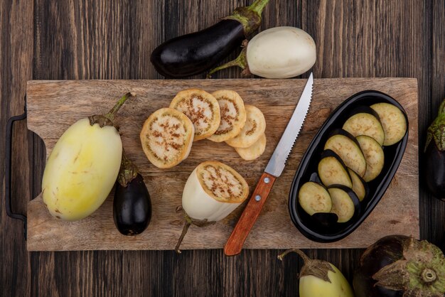 Bovenaanzicht zwart-wit aubergine plakjes op snijplank met mes op houten achtergrond