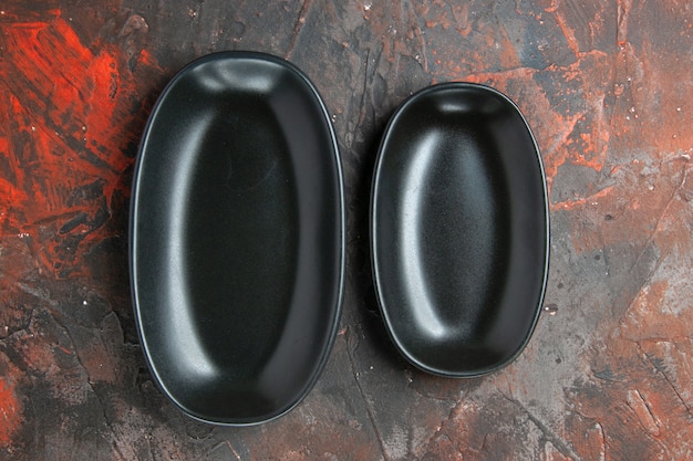 Bovenaanzicht zwarte ovale borden groot en klein formaat op donkerrode achtergrond