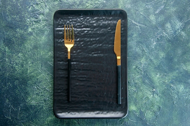 bovenaanzicht zwarte plaat met gouden vork en mes op donkere achtergrond kleur diner bestek maaltijd restaurant utencil food