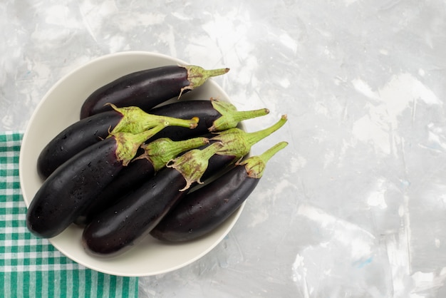 Bovenaanzicht zwarte rauwe aubergines in witte plaat op de lichte achtergrond groenten verse rauwkost maaltijd boom