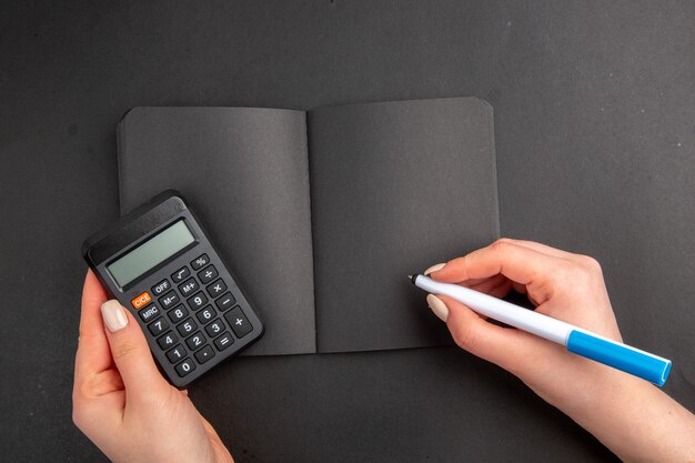 Bovenaanzicht zwarte rekenmachine en pen in vrouwelijke notitieblok op zwarte tafel
