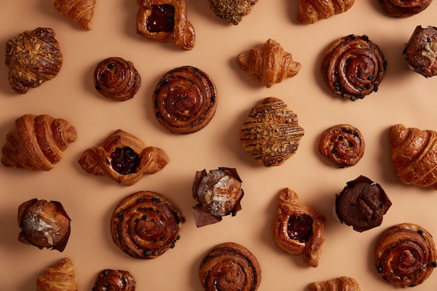 Bovenstaand shot van smakelijke, smakelijke zoetwaren om je zoetekauw te bevredigen. Gebak met vullingen en rozijnenbroodjes, chocolademuffins, croissants op beige achtergrond. Verse bakkerijproducten met veel calorieën