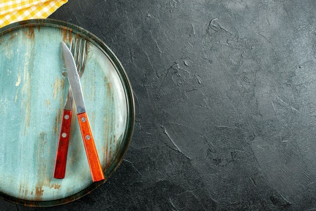 Bovenste halve weergave mes en een vork op plaat geel en wit geruit servet op donkere grond met vrije ruimte