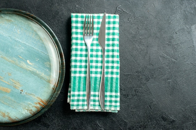 Bovenste halve weergave ronde schotel diner mes en vork op groen en wit geruit servet op zwarte tafel kopie plaats