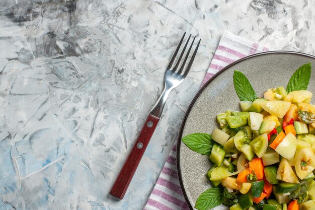 Gratis foto bovenste helft groene tomatensalade op ovale plaat een vork op donkere achtergrond