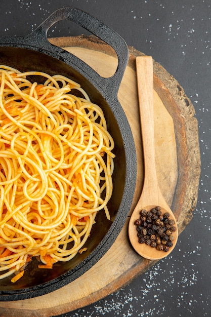 Bovenste helft spaghetti in koekenpan houten lepel op houten bord op donkere ondergrond