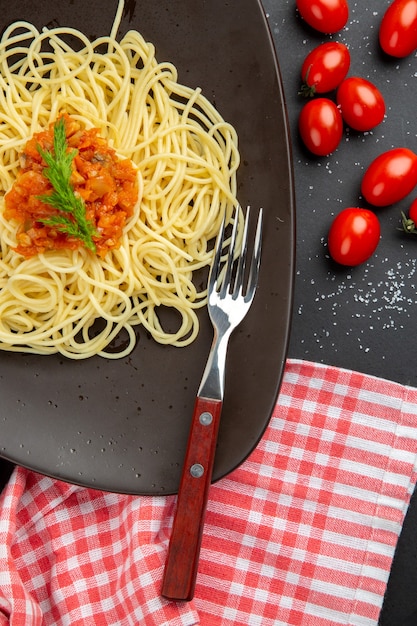 Bovenste helft spaghetti met saus op plaatvork cherrytomaatjes op zwarte tafel