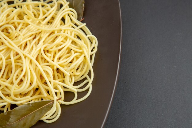 Bovenste helft spaghetti pasta met laurierblaadjes op plaat op zwarte ondergrond