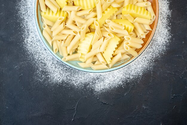 Bovenste helft uitzicht penne pasta met aardappel in kom bestrooid met bloem op donker