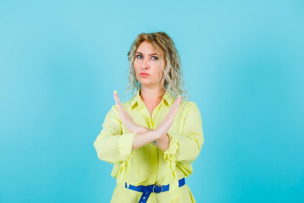 Boze blonde vrouw toont stopgebaar door handen op blauwe achtergrond te kruisen