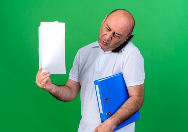 Boze casual volwassen man spreekt over telefoon en map met papier te houden