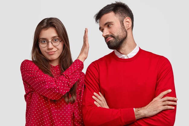 Boze Europese vrouw in rode blouse maakt weigeringsgebaar, houdt palm voor het gezicht van vriendjes