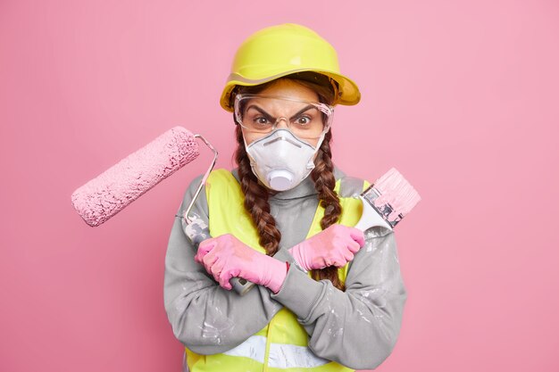 Boze geïrriteerde vrouwelijke bouwer kruist armen houdt reparatiegereedschap klaar voor handmatig werk dat betrokken is bij het verbouwen van huizen