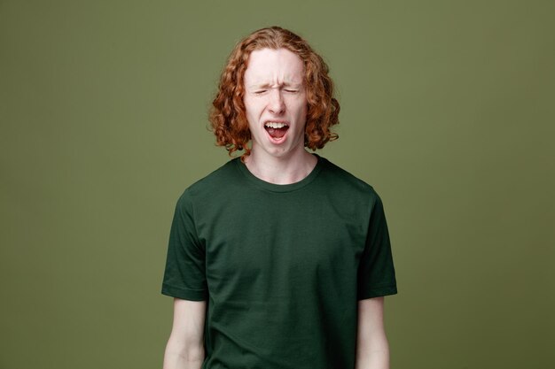 Boze jonge knappe kerel die groen t-shirt draagt dat op groene achtergrond wordt geïsoleerd