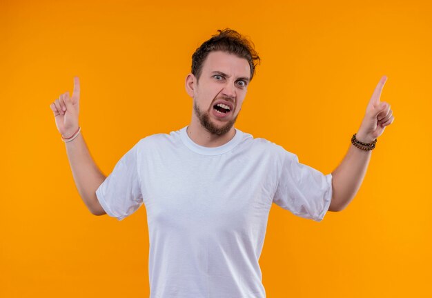 Boze jonge man met een wit t-shirt wijst naar boven op geïsoleerde oranje muur