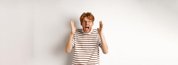 Boze jonge man met rood haar schreeuwend naar de camera schreeuwend en verontwaardigd kijkend handen schudden standi