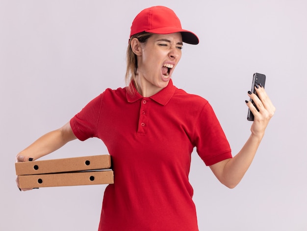 Boze jonge mooie levering meisje in uniform houdt pizzadozen en kijkt naar de telefoon op wit