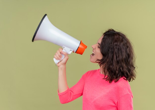 Boze jonge mooie vrouw die door spreker spreekt die zich in profielmening over geïsoleerde groene muur bevindt