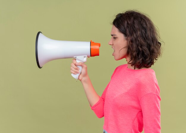 Boze jonge mooie vrouw die door spreker spreekt die zich in profielmening over geïsoleerde groene muur bevindt