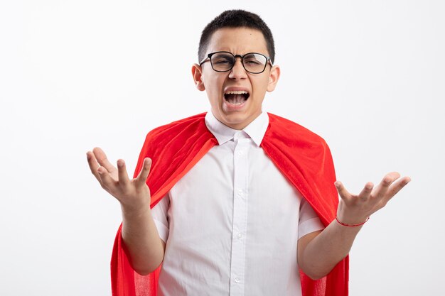 Boze jonge superheld jongen in rode cape bril kijken camera weergegeven: lege handen geïsoleerd op een witte achtergrond