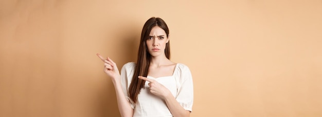 Boze jonge vrouw fronst met de vingers naar rechts en klaagt teleurgesteld over het opstaan van het logo