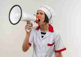 Gratis foto boze jonge vrouwelijke kok in eenvormige chef-kok die in luide spreker schreeuwt die kant bekijkt die op wit wordt geïsoleerd