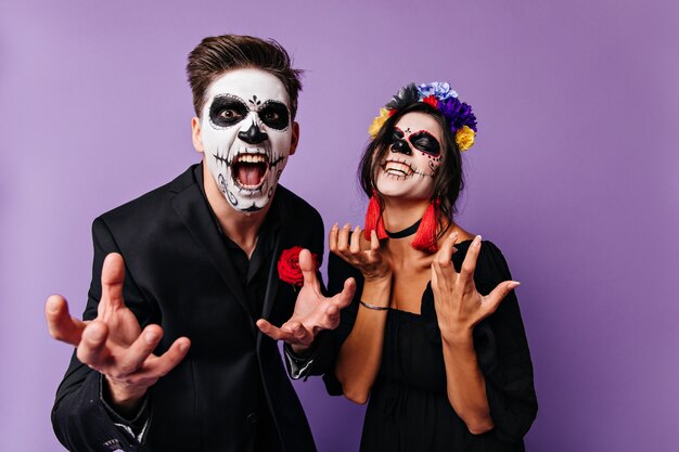 Boze jongen en meisje in maskers van de schedel poseren emotioneel en willen hun grootsheid tonen. Portret van donkerharige Mexicaans paar.