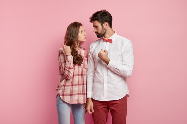 Boze man en vrouw kijken elkaar streng aan, tonen vuisten, hebben ruzie, gekleed in een stijlvolle outfit, zoeken relaties uit