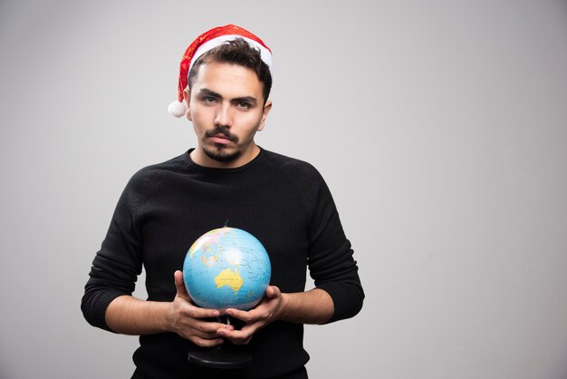 Boze man in de hoed van de Kerstman met een wereldbol.