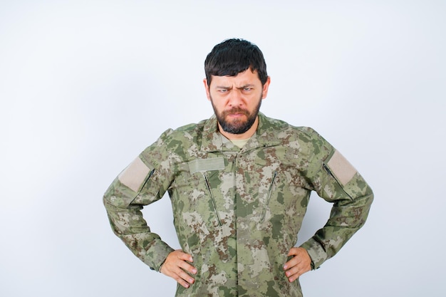 Boze militaire man kijkt naar de camera door de handen op de taille te zetten op een witte achtergrond