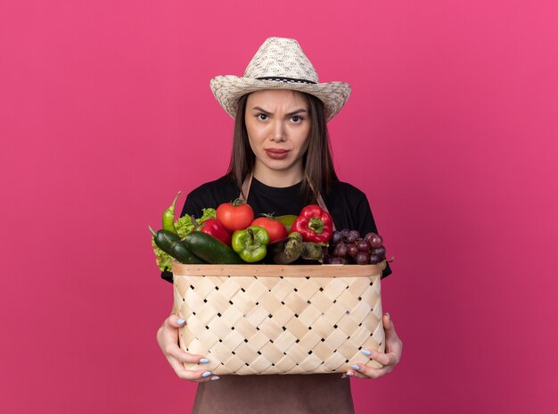 Boze mooie blanke vrouwelijke tuinman die een tuinhoed draagt met een groentemand