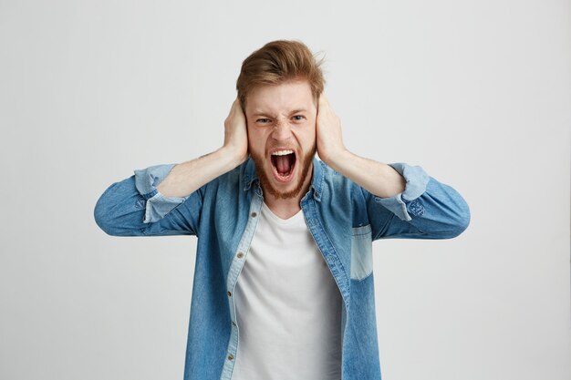 Boze woede jonge man met baard schreeuwen schreeuwende oren sluiten.