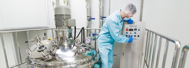 Breedbeeld wetenschapper in blauw laboratoriumpak check bedieningspaneel in de buurt van grote verchroomde tanks